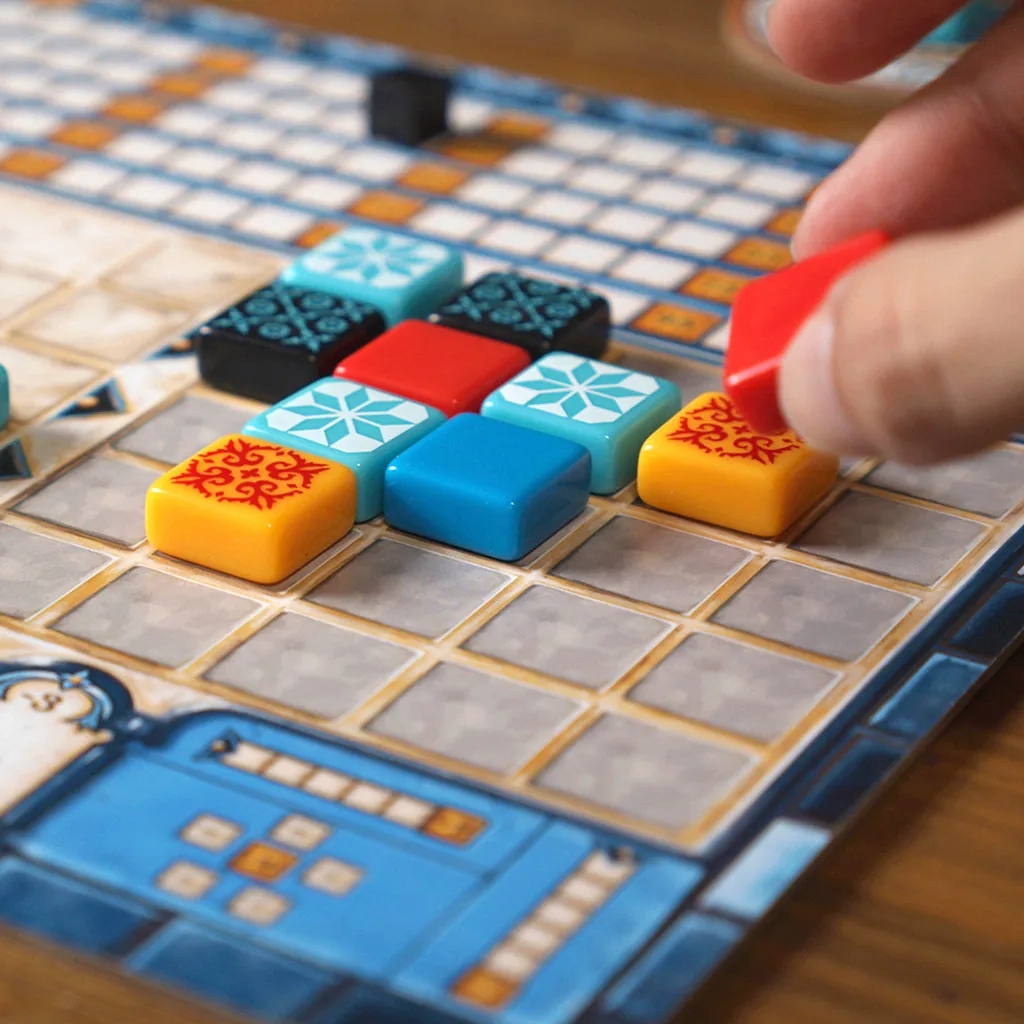 A hand placing a red tile on a player board with tiles already lined up in rows