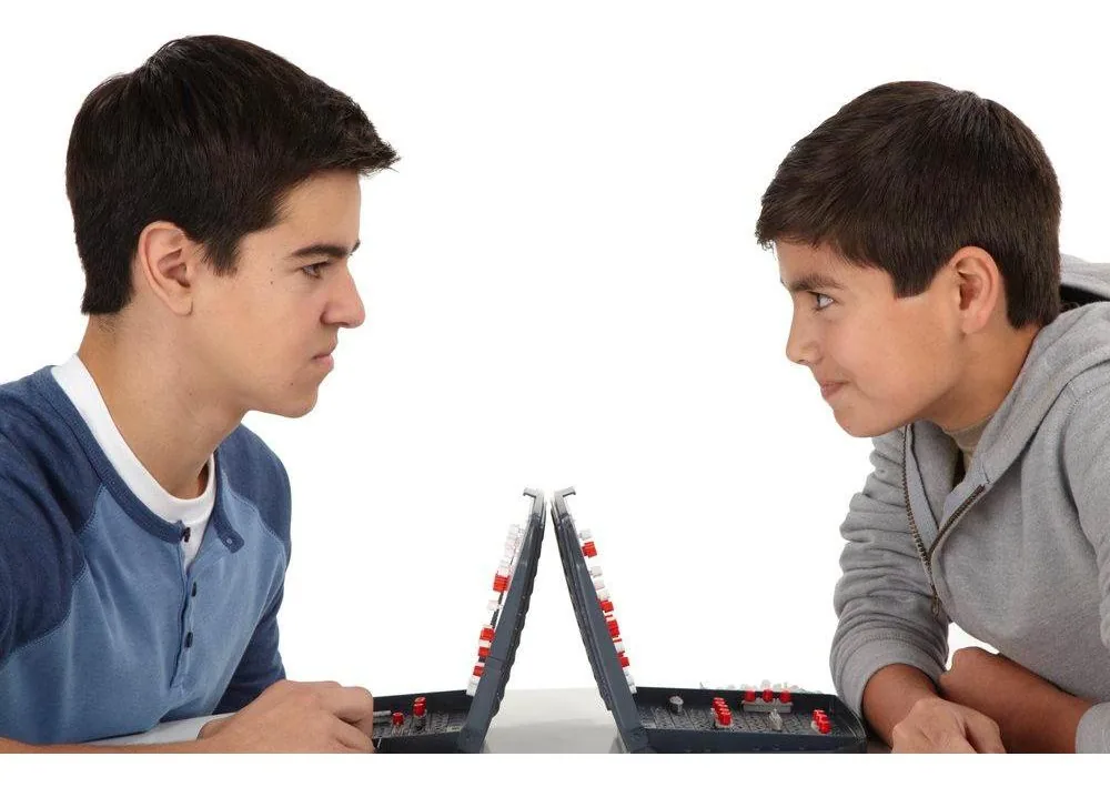 Two boys facing each other across their open Battleship cases