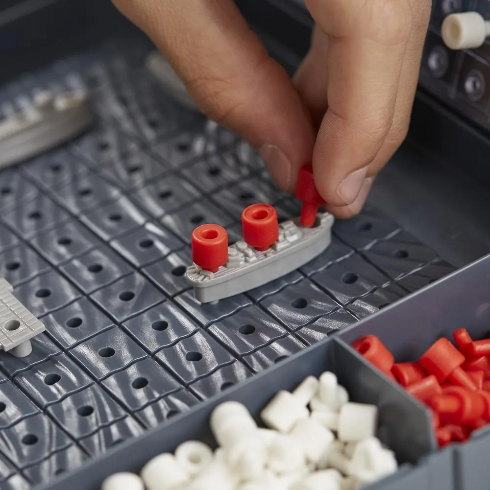 Fingers placing a red hit peg on a ship, with white miss pegs in the tray