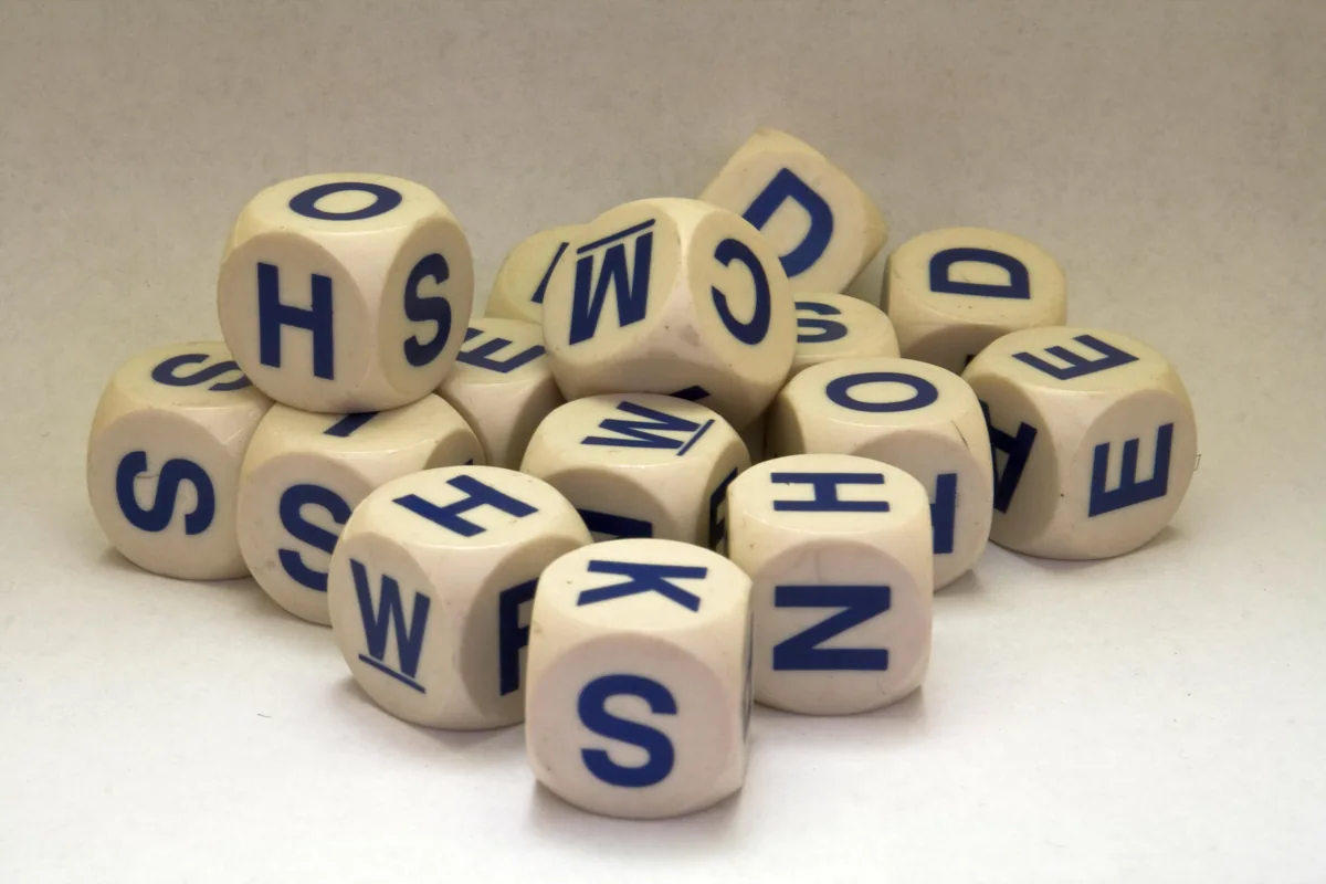 A pile of white Boggle letter cubes with blue letters