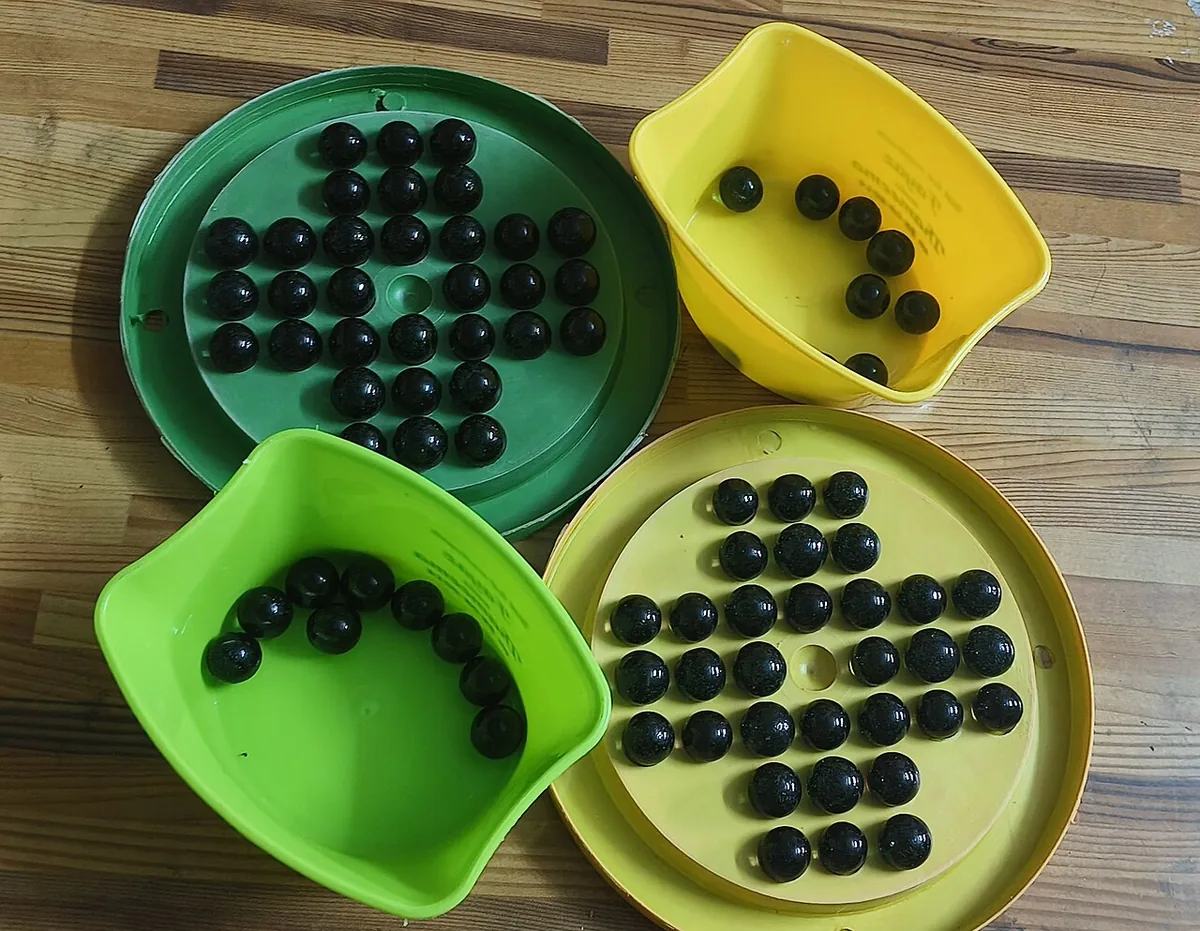 Plastic Brainvita boards and trays in green and yellow, with black marbles