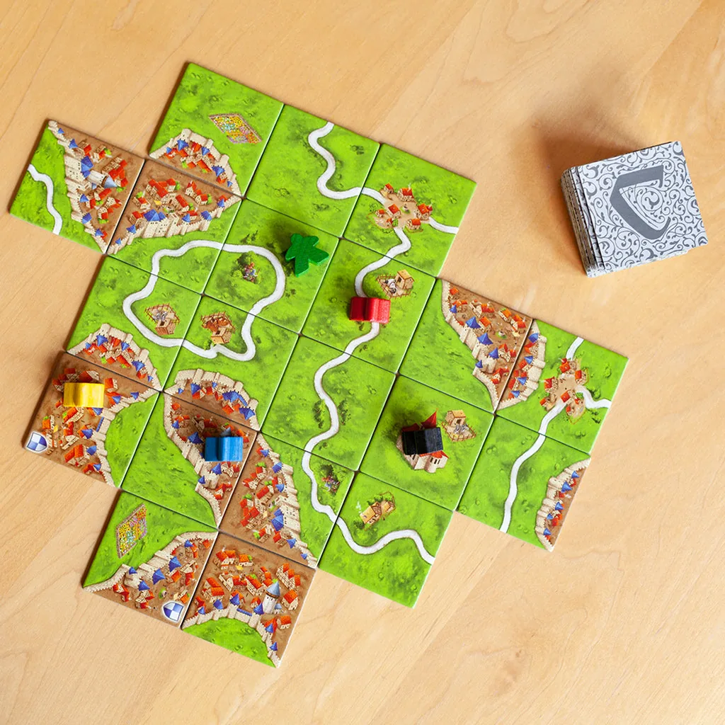 A map of tiles on a light wooden table with meeples placed, seen from above