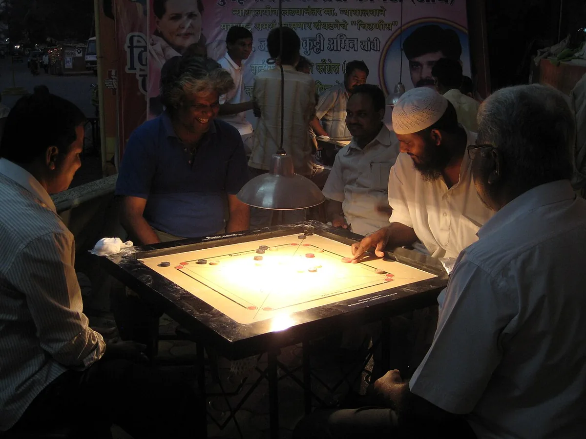 Four men playing carrom at night under a lamp in Andheri, Mumbai, with others watching
