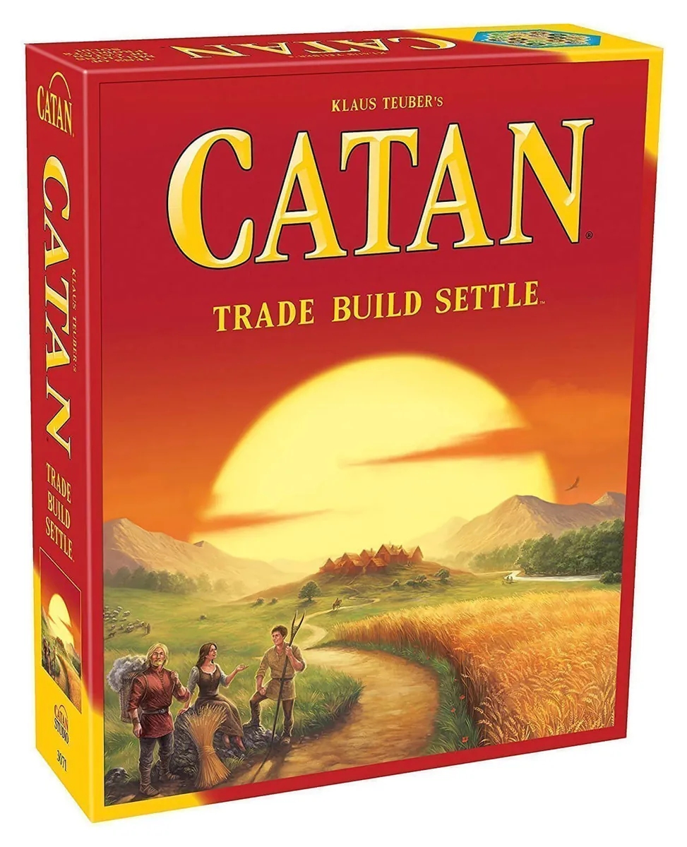 The Catan box seen at an angle: red and yellow box with the gold CATAN title, 'Trade Build Settle', and a painting of a sunset over wheat fields with three settlers on a path