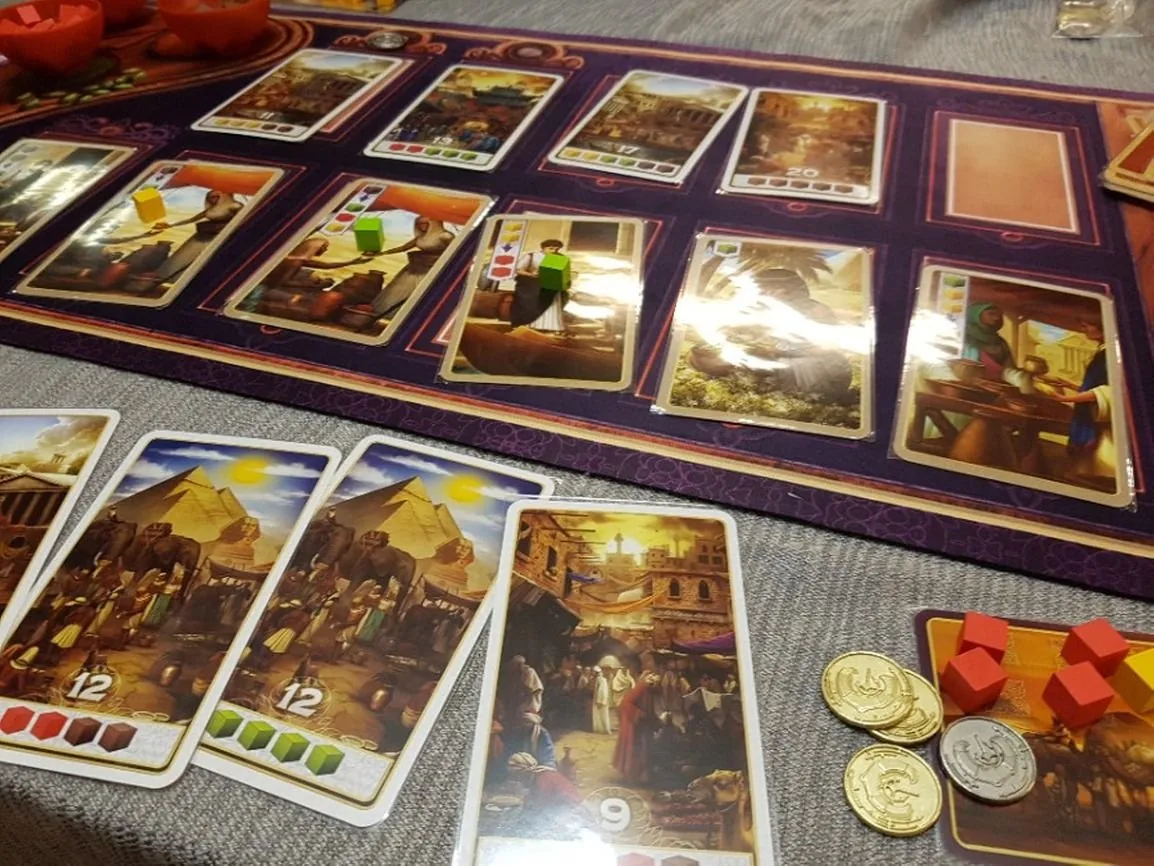 A row of merchant and point cards on a table with spice cubes and coins