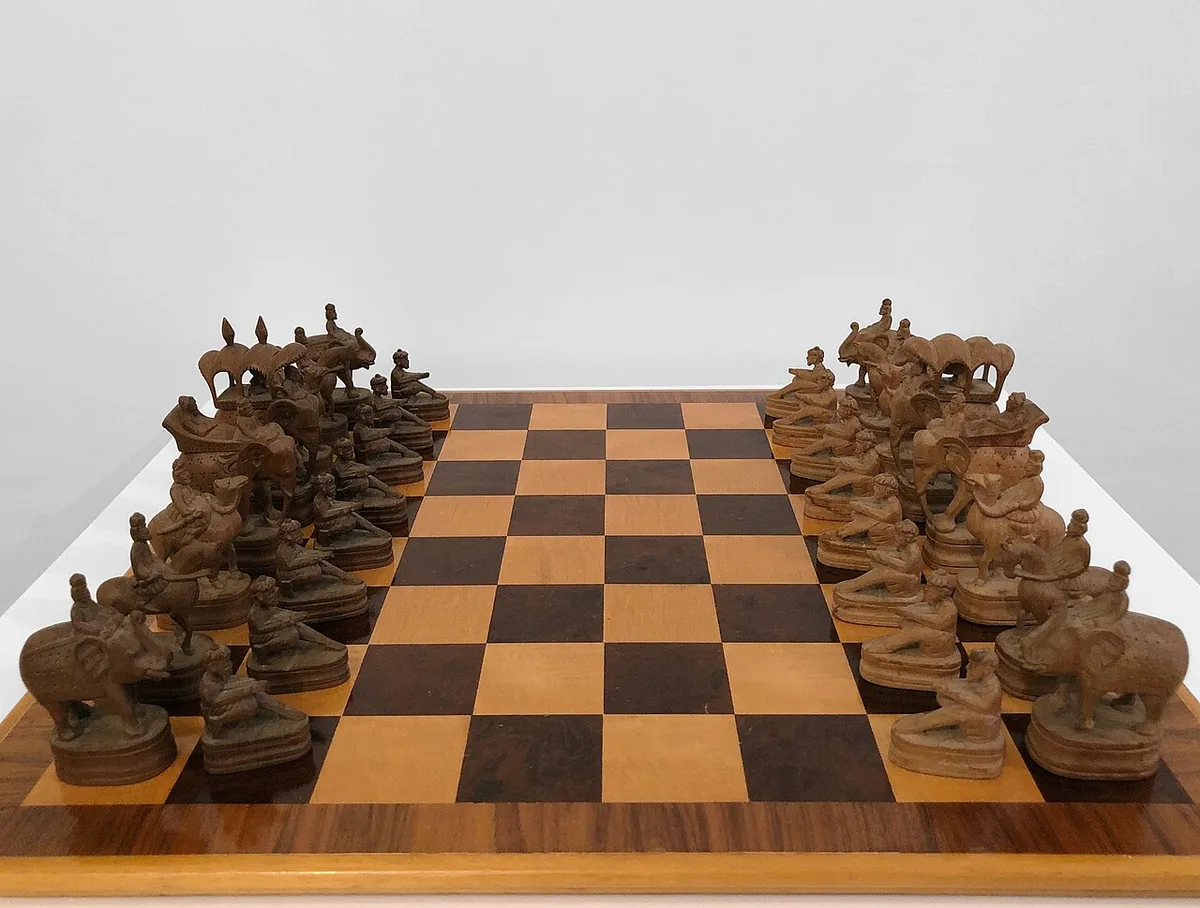 A carved wooden chaturanga set laid out on a board, with elephants, horses and chariots