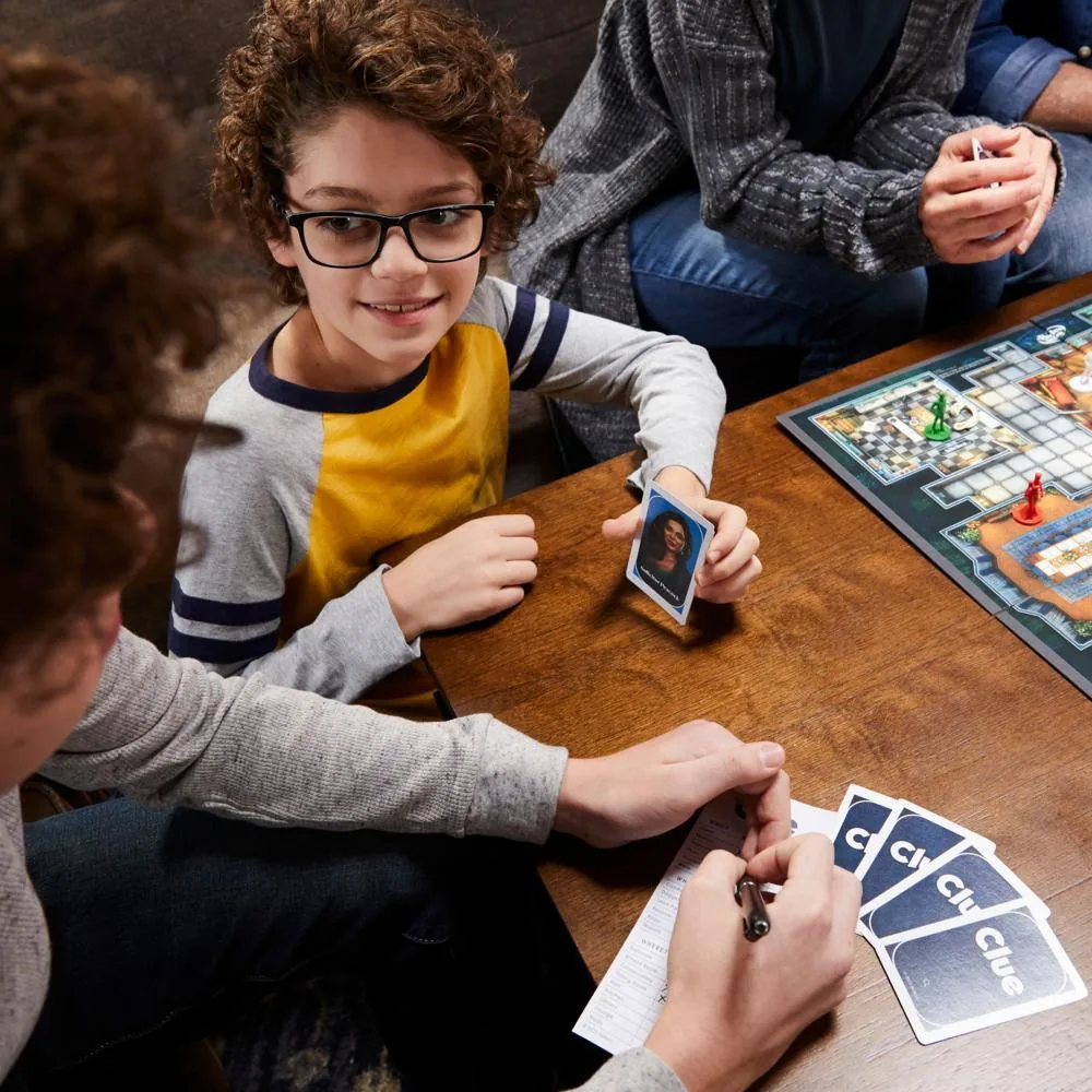 A boy holding his Cluedo cards close while another player reaches across the table