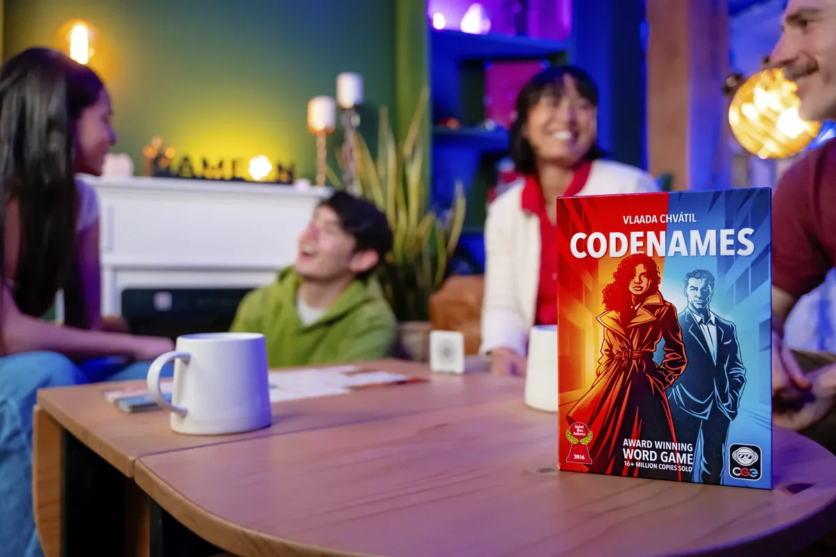 Friends laughing on a sofa during a game, with the Codenames box on the table