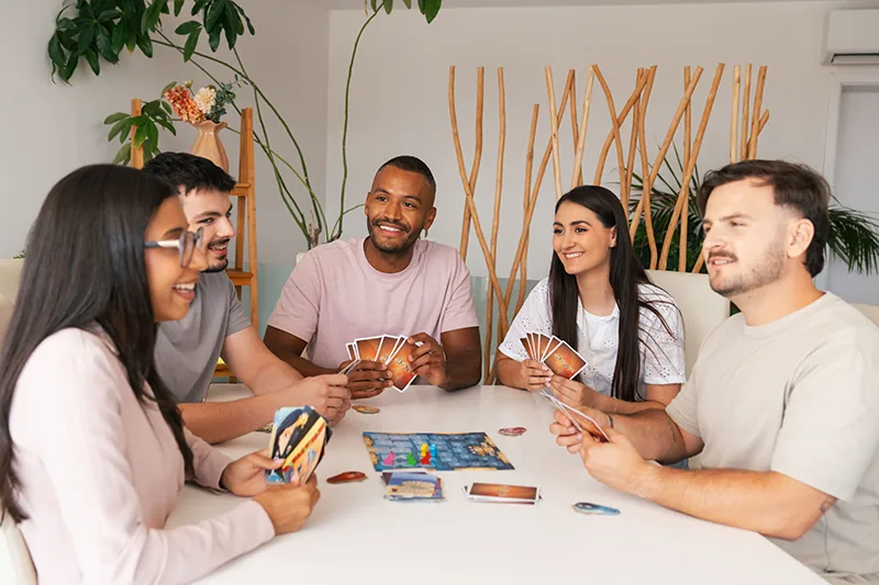 Five friends round a table holding Dixit cards and laughing