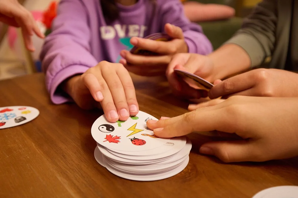 Hands reaching for a pile of round Dobble cards