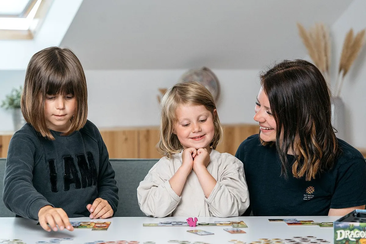 Two young girls and a woman playing Dragomino at a table