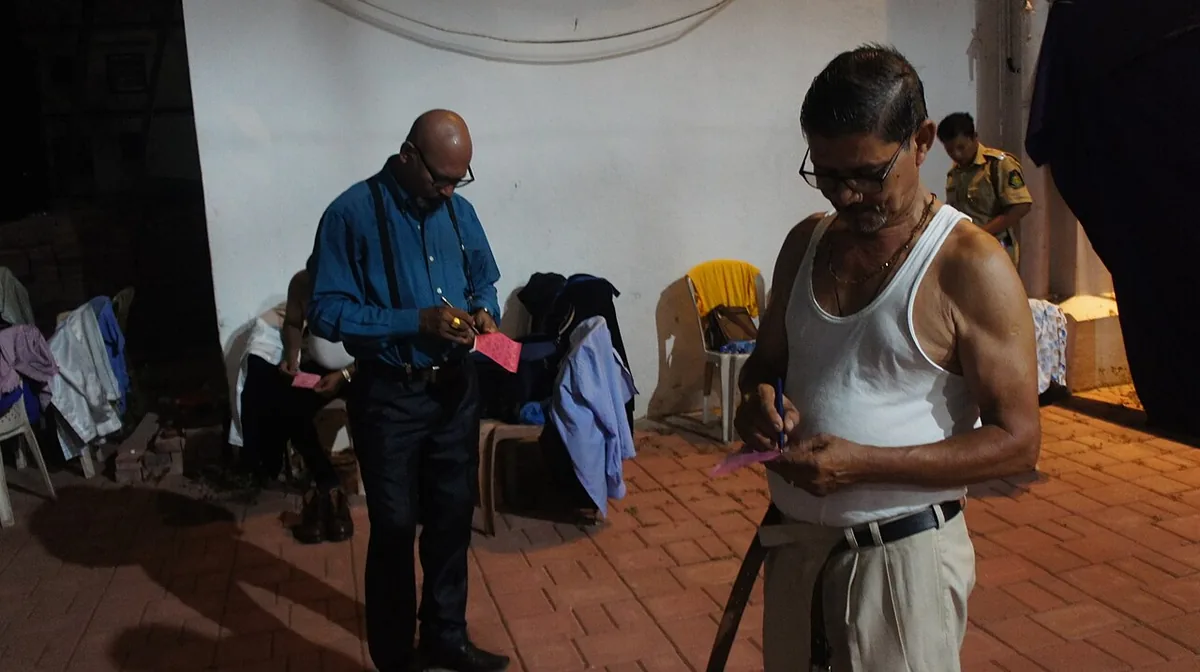 Konkani theatre actors in Goa standing in a hall and checking their housie tickets during the interval