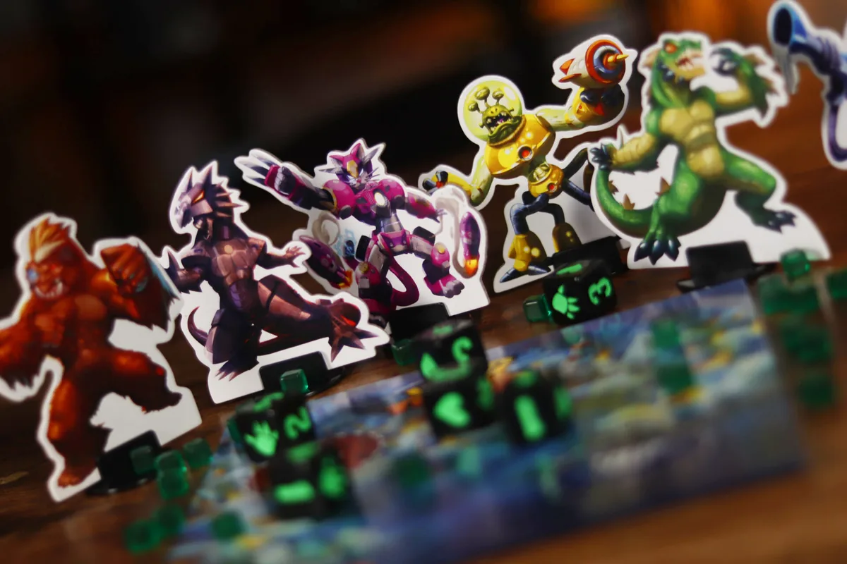 Six monster figures lined up behind black dice and green energy cubes
