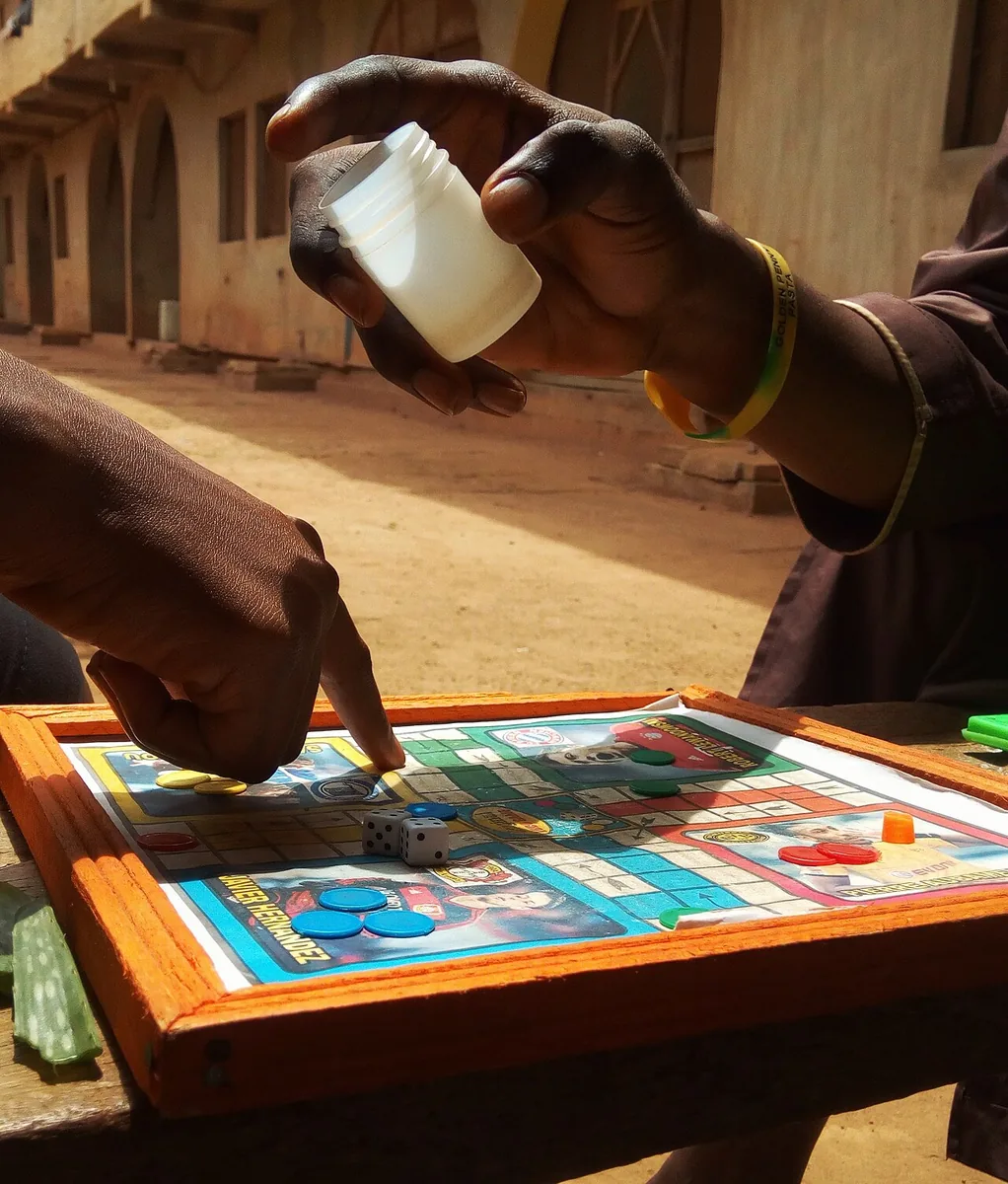 Hands rolling the die from a cup over a Ludo board on a small wooden table