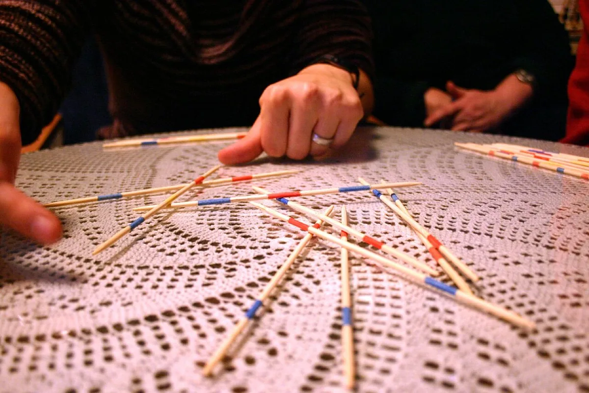 A hand gently lifting one stick from a scattered pile of Mikado sticks on a lace tablecloth