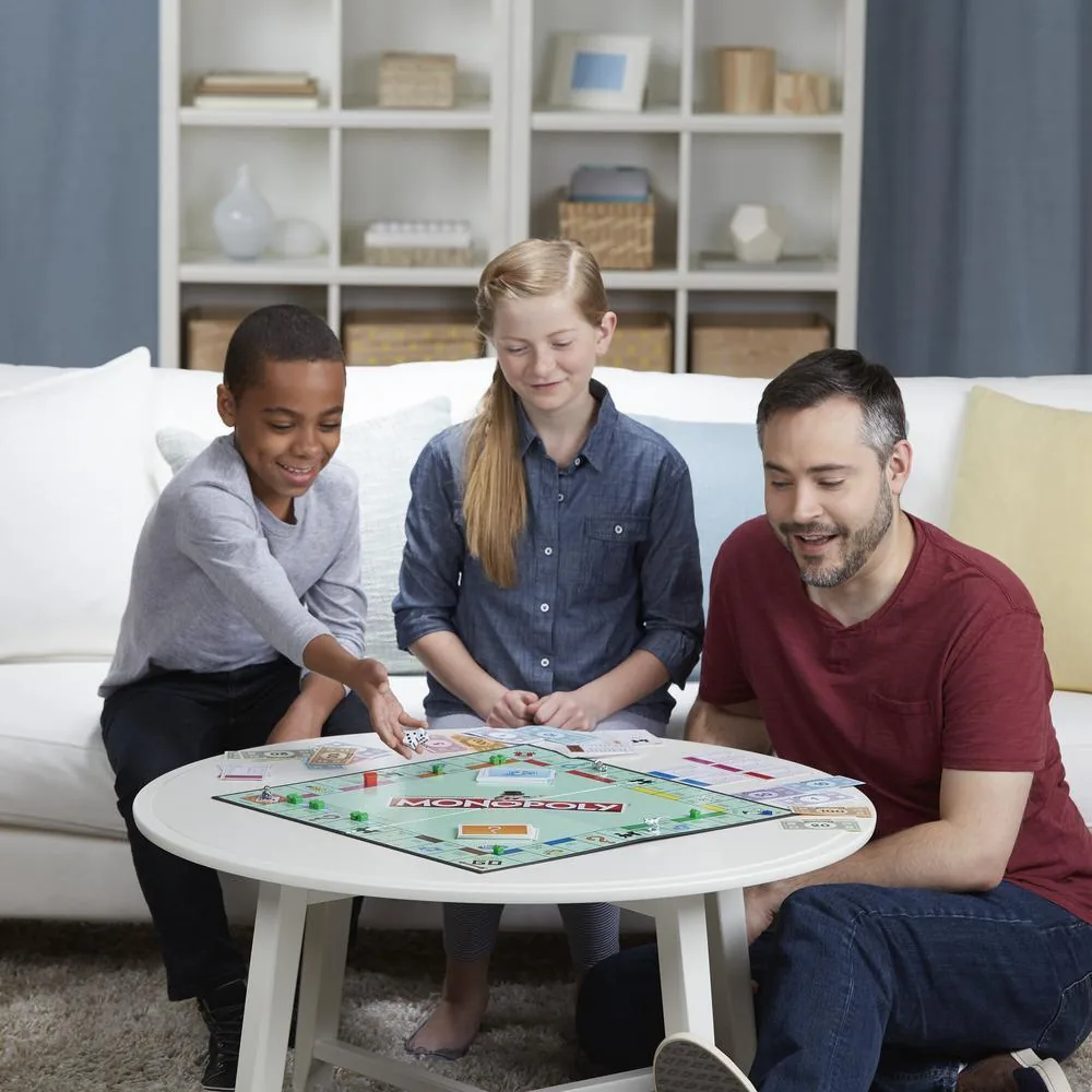A man and two children playing Monopoly at a low white table in a living room