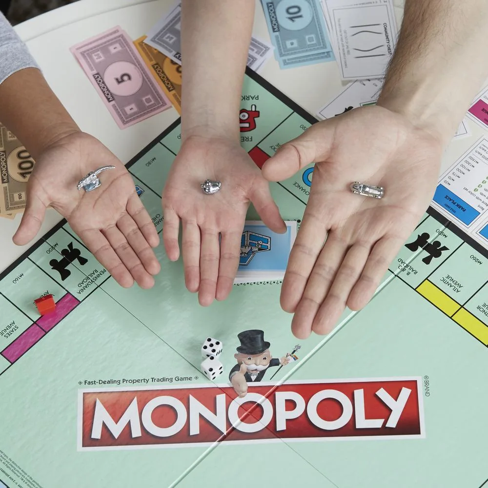 Three open hands holding metal Monopoly tokens over the board