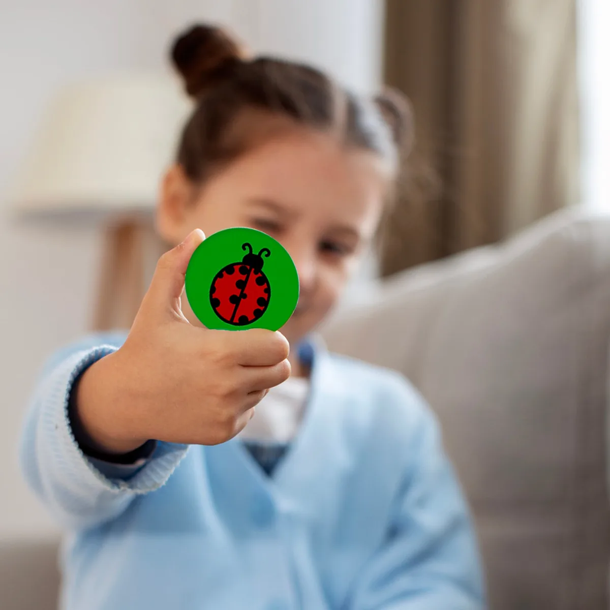 A young girl holding up a round green token with a ladybird picture