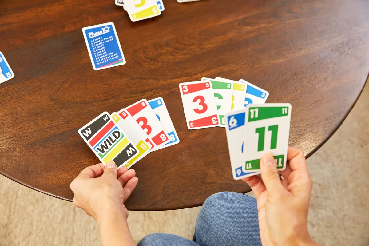 Hands laying down Phase 10 number cards on a wooden table