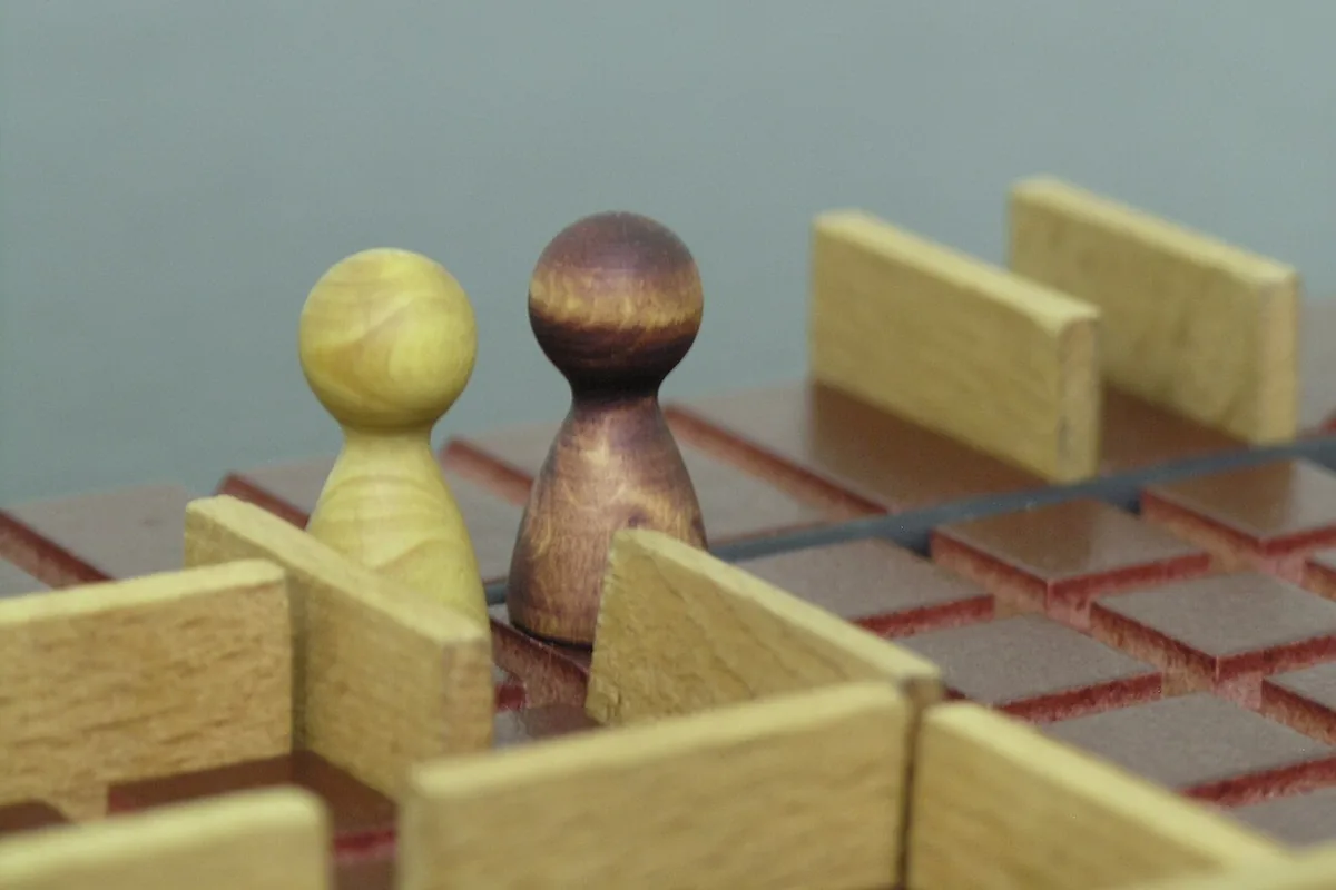 Two wooden pawns between light wooden walls on a Quoridor board
