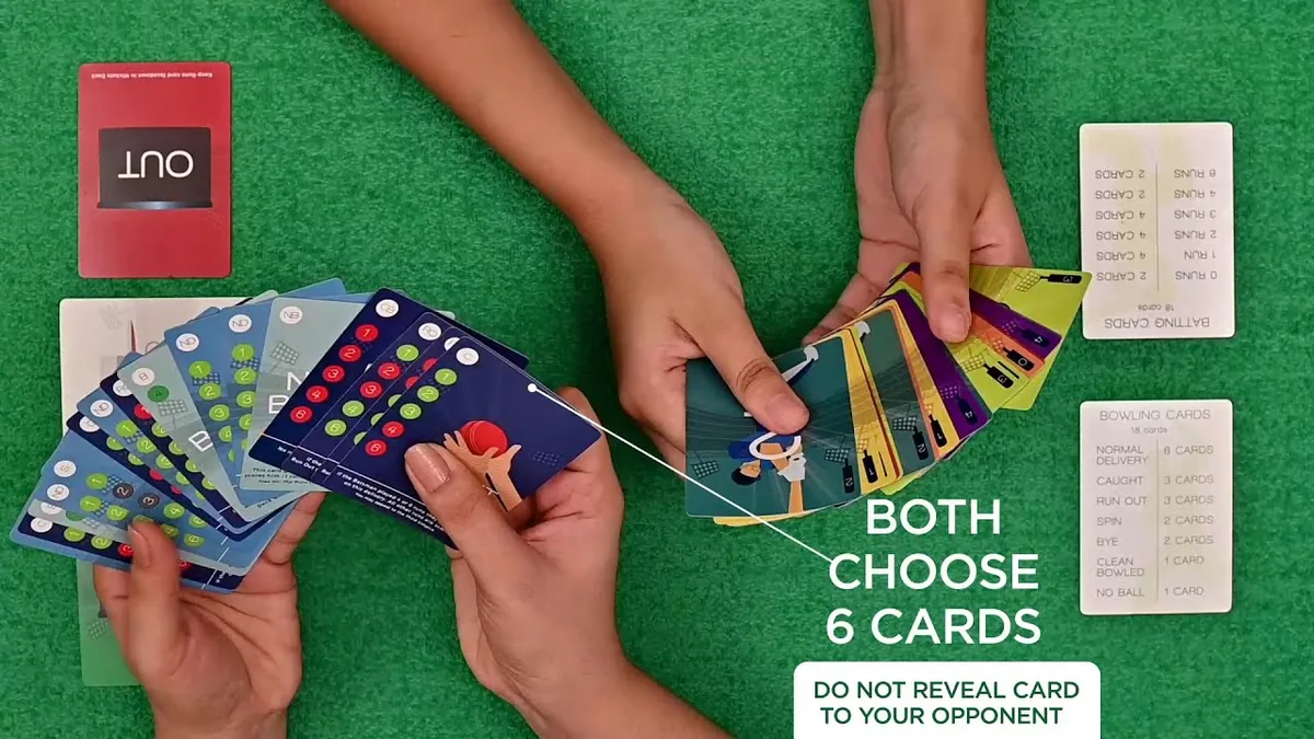 Two players' hands choosing six cards each over a green table, with Out, Not Out and reference cards laid out (still from Binca's video)