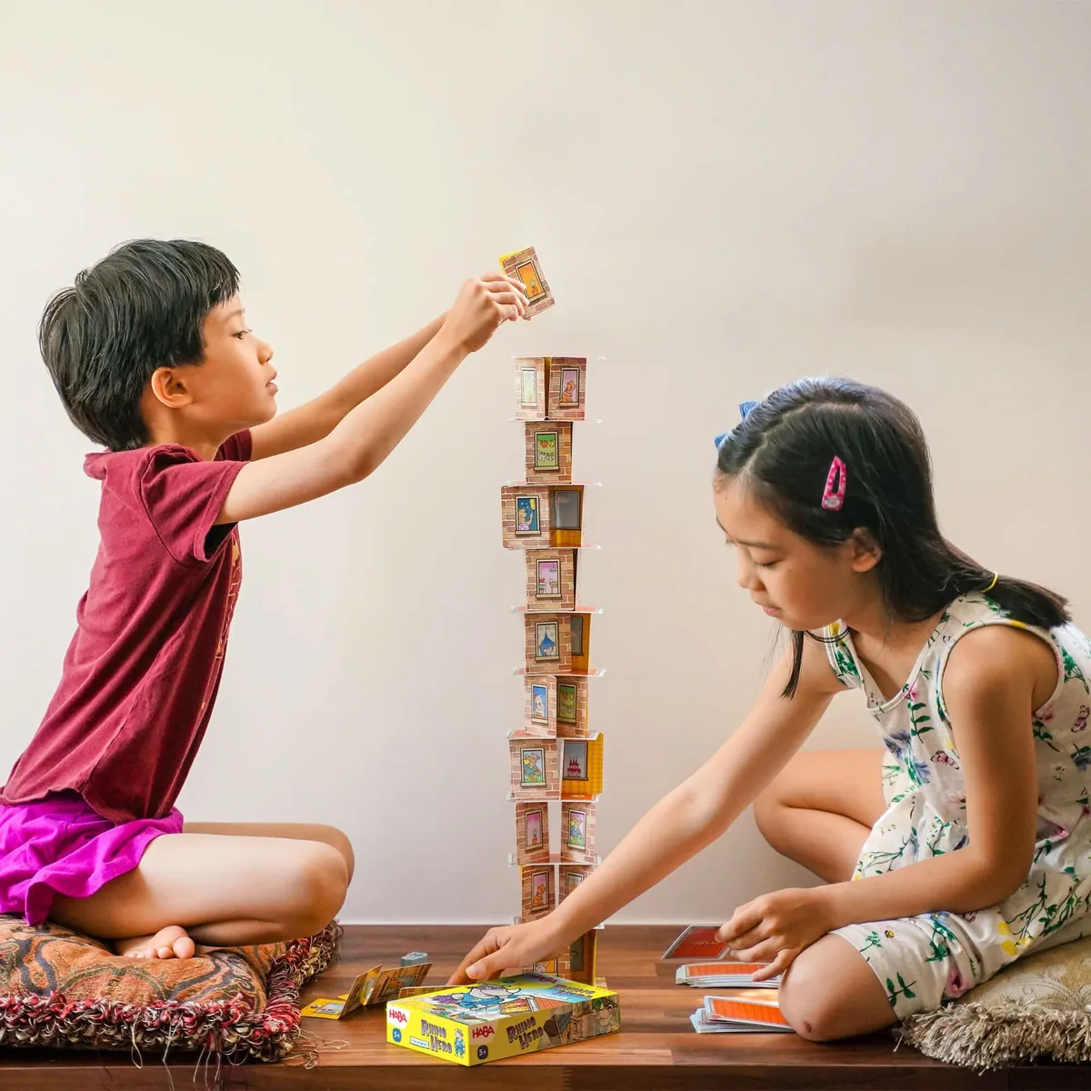 Two children taking turns to build a Rhino Hero card tower.