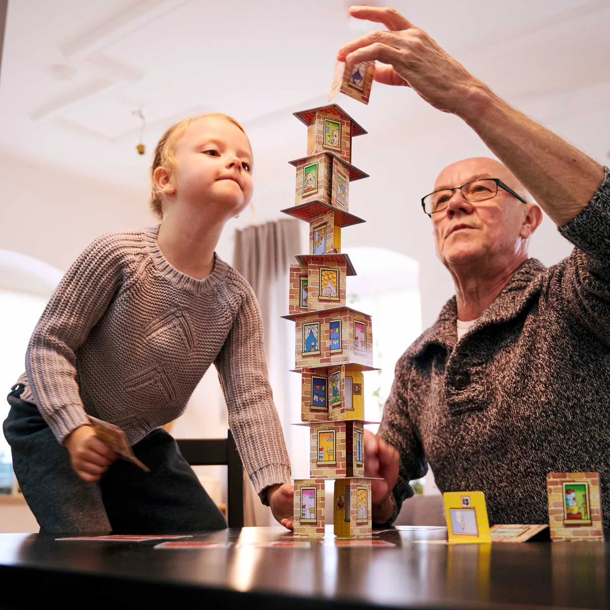 A girl and an older man reaching up to a very tall Rhino Hero tower on a table