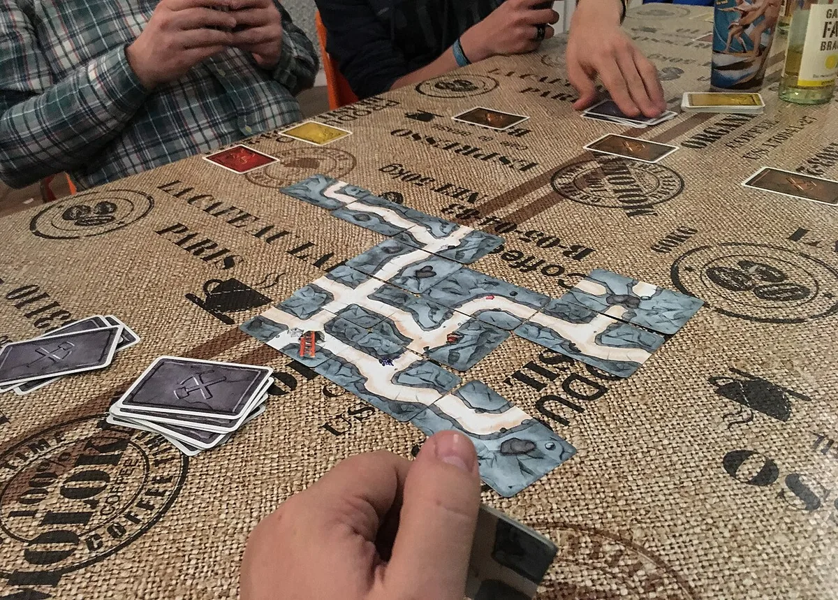 Players' hands over a winding tunnel of Saboteur path cards laid across a table