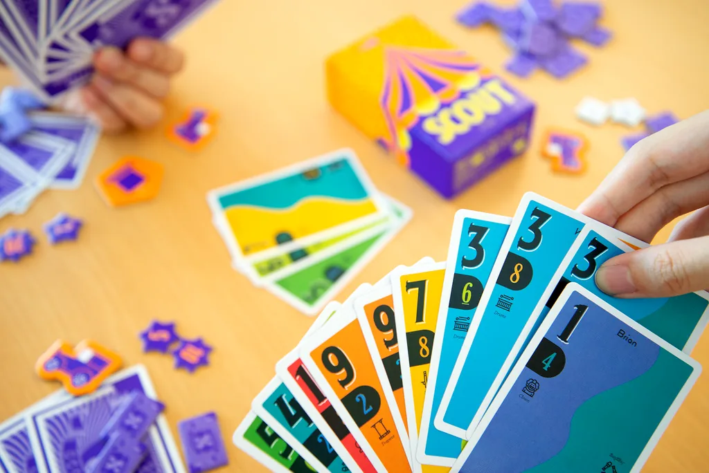 A hand holding a fan of SCOUT cards over the table, with Scout chips scattered around