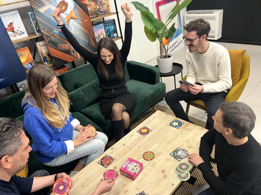 A player throwing her arms up in triumph as the others react around the table