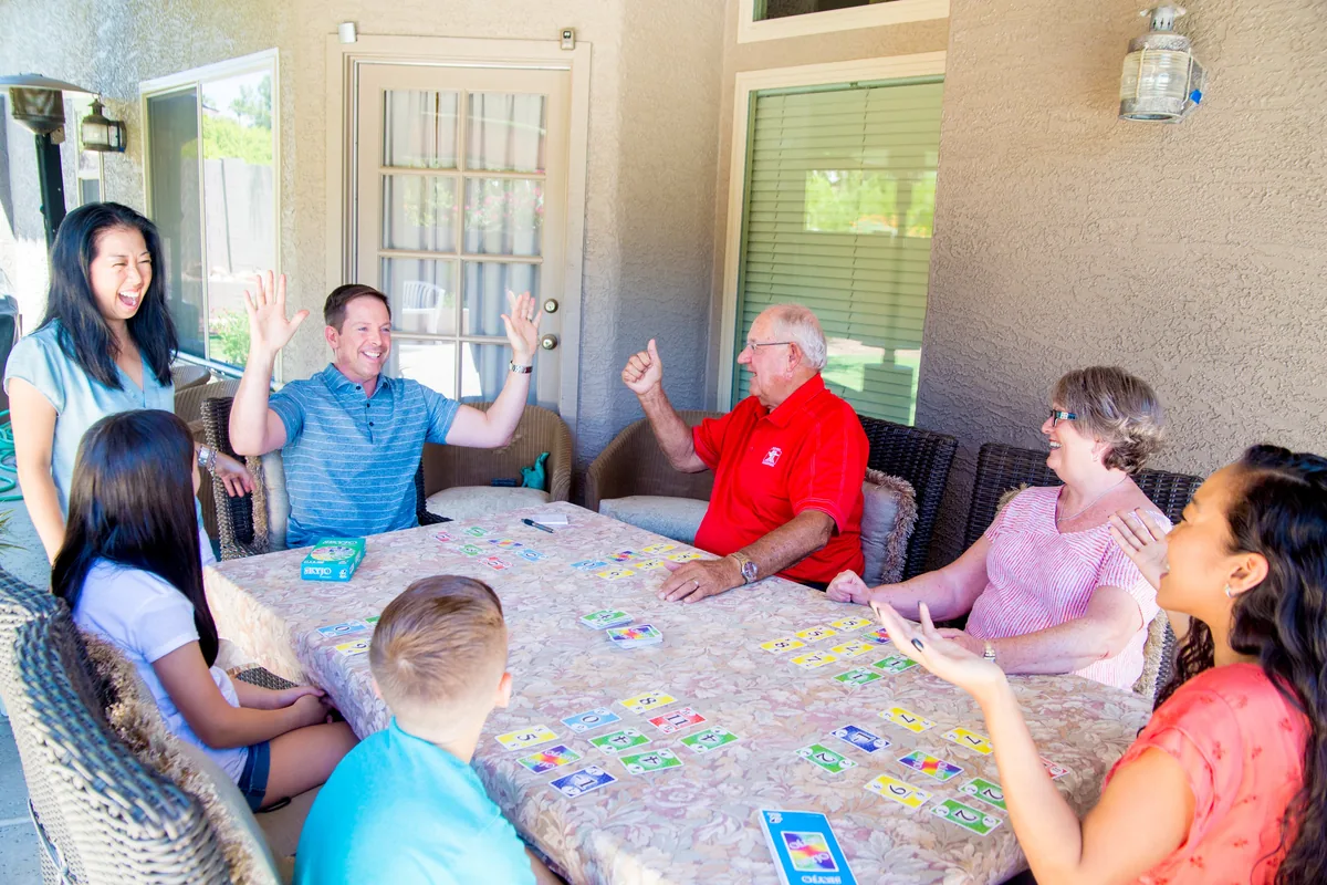 A family of all ages laughing around a table covered in SKYJO cards