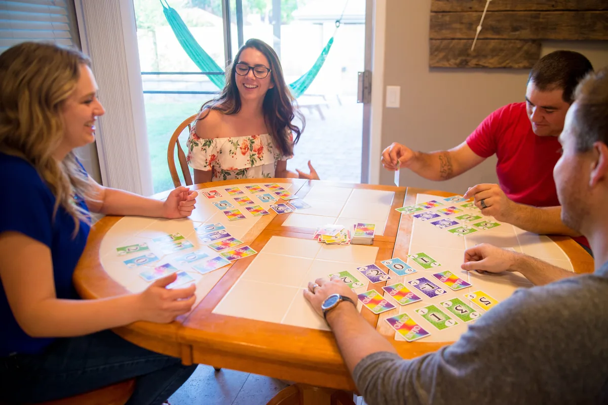 Friends at a round table playing SKYJO, each with a grid of cards
