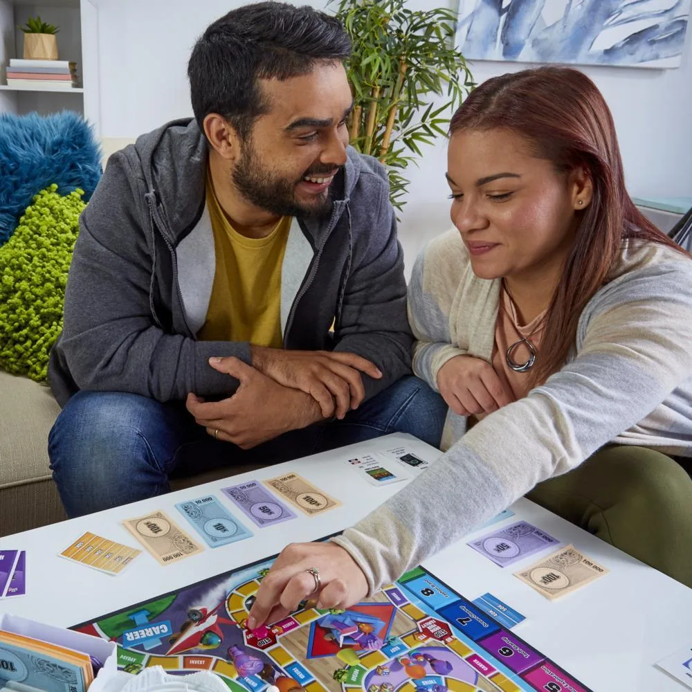 A man and a woman smiling as one of them moves a car along the board