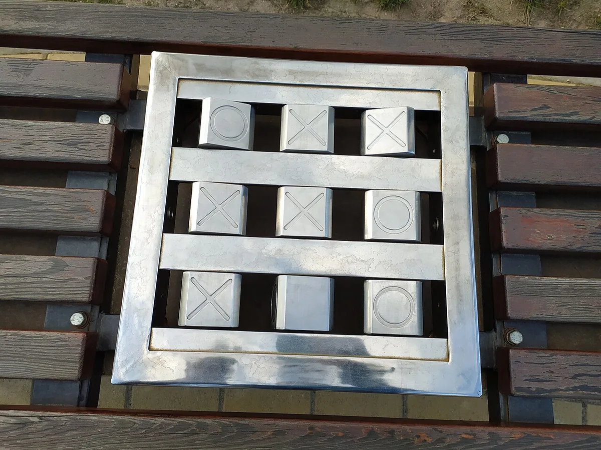 A metal tic-tac-toe built into a park bench, with turning blocks marked with crosses and zeros
