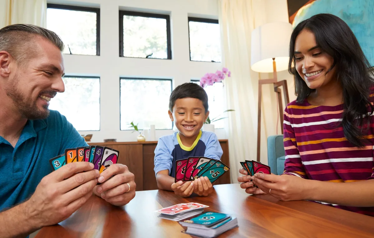 A father, mother and son laughing at a table as they play UNO Flip