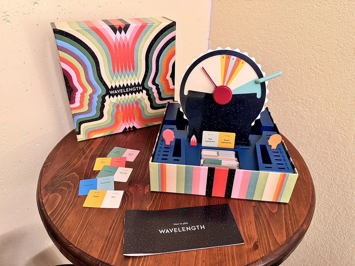 Wavelength set up at home on a round wooden table: the box, the device in its tray, spectrum cards and the rulebook