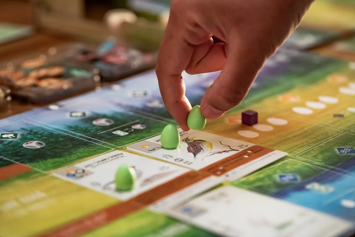 A hand placing a green egg on a bird card on a player mat